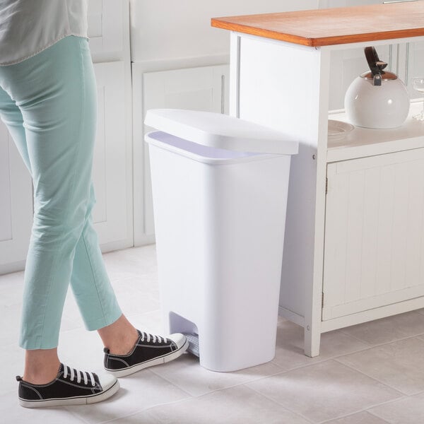 A white rectangular step-on wastebasket placed next to a kitchen counter.