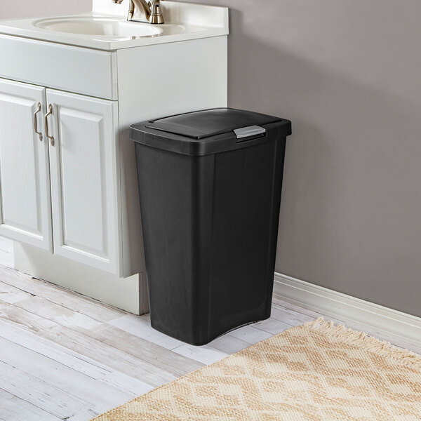 A black rectangular 13-gallon wastebasket with a lid, placed next to a bathroom sink cabinet.