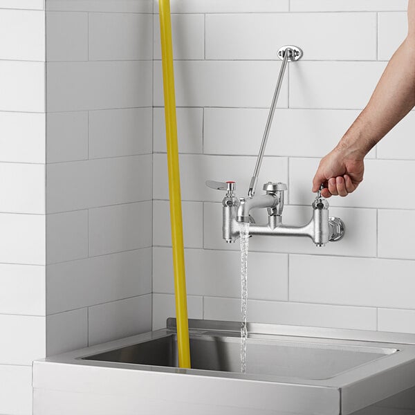 A person using a T&S wall mount mop sink faucet to fill a yellow mop sink hose.