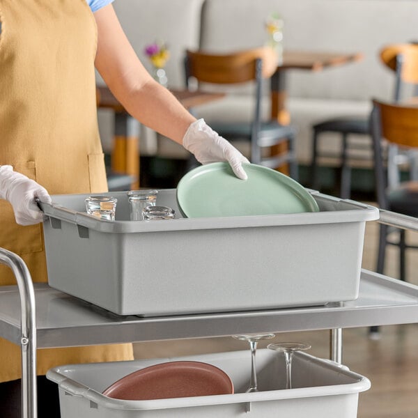 A gray heavy duty polyethylene plastic bus tub filled with dishes and glasses on a cart in a restaurant setting.