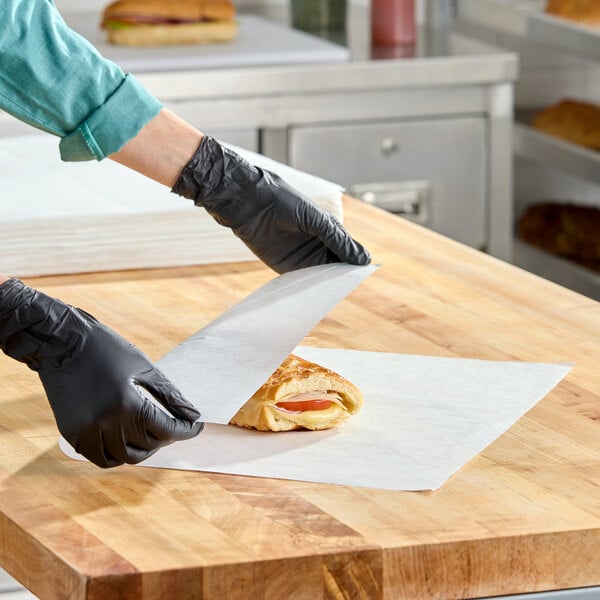 A sheet of Choice 18" x 18" insulated deli wrap paper being used to wrap a sandwich on a wooden countertop.