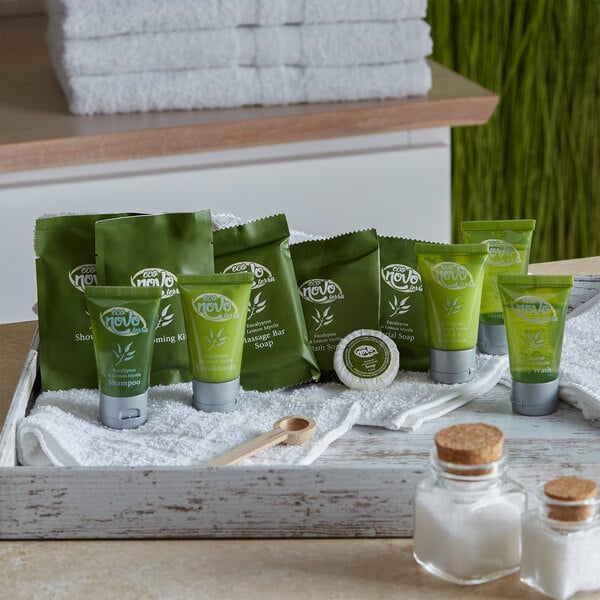 An 11-piece hotel amenity toiletries kit featuring various green-packaged personal care products, displayed on a white tray with towels.