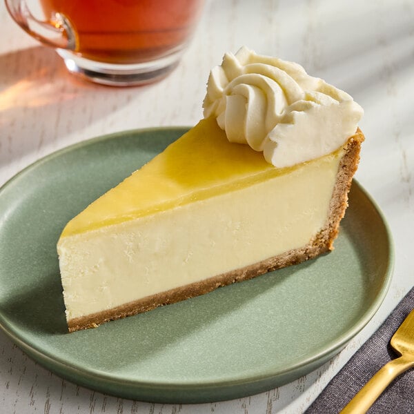 A slice of key lime pie cheesecake with a graham cracker crust and a dollop of whipped cream on top, served on a green plate.