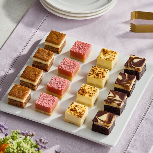 A tray of assorted pre-cut cheesecake squares in various flavors and colors, arranged neatly on a white platter.