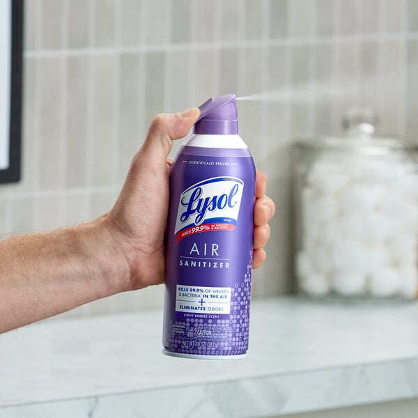 A can of Lysol Light Breeze Scent Air Sanitizer Spray being used in a bathroom setting.