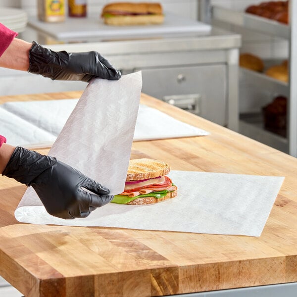 A sheet of insulated deli wrap paper being used to wrap a sandwich on a wooden countertop.
