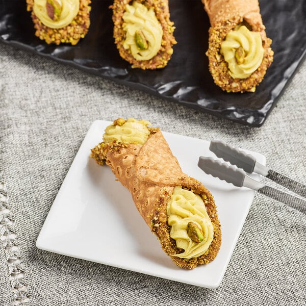 A pistachio cannoli filled with pistachio cream and garnished with crushed pistachios on a white plate.