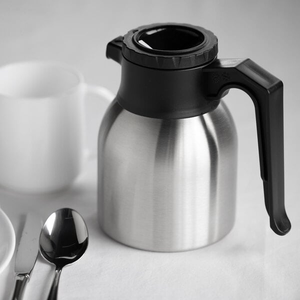 A stainless steel insulated coffee server with a black handle and lid.