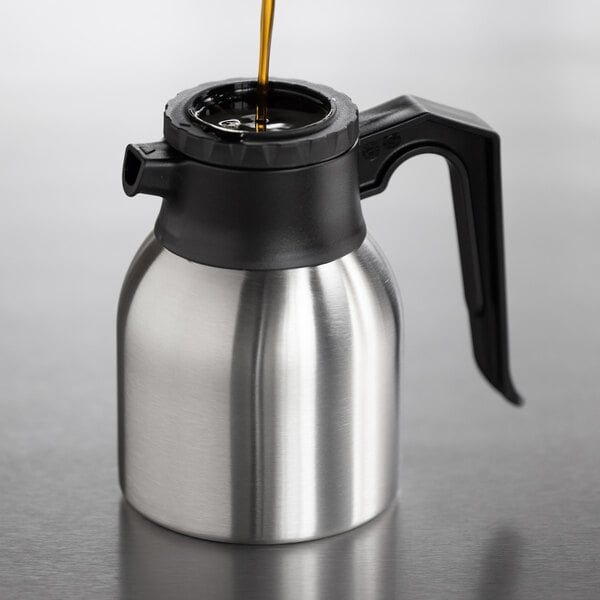 A stainless steel insulated coffee server with a black handle and lid, being filled with liquid.