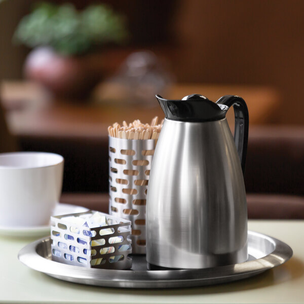 A stainless steel insulated coffee carafe with a black lid, placed on a tray with coffee accessories.