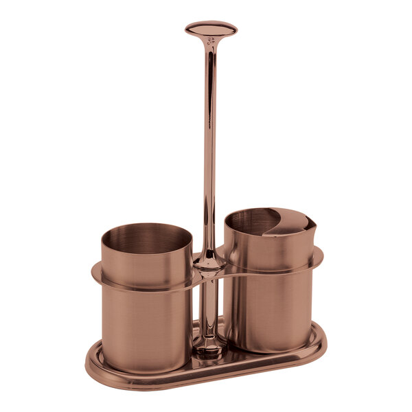A rose gold stainless steel sugar stick holder and creamer set with a central handle.
