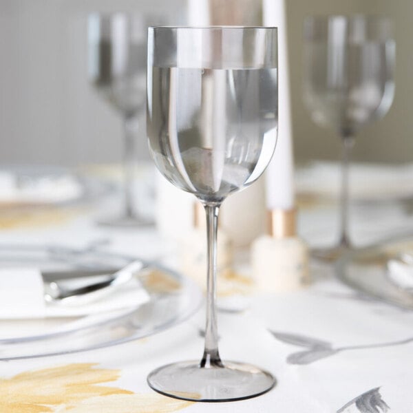 A clear smoke-colored plastic wine goblet filled with water, placed on a set dining table.