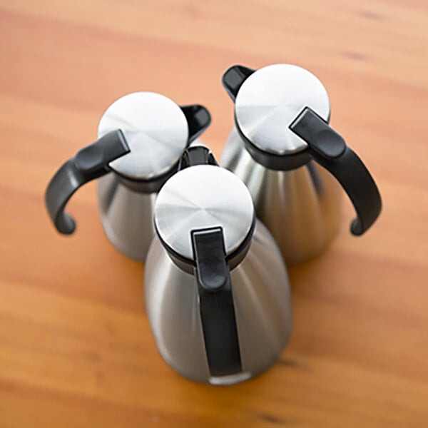 A set of three stainless steel insulated coffee servers with black push button lids and handles.