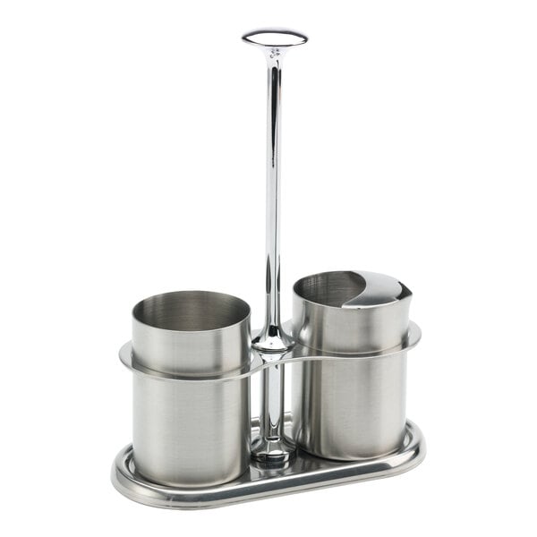 A brushed stainless steel sugar stick holder and creamer set with a central handle.