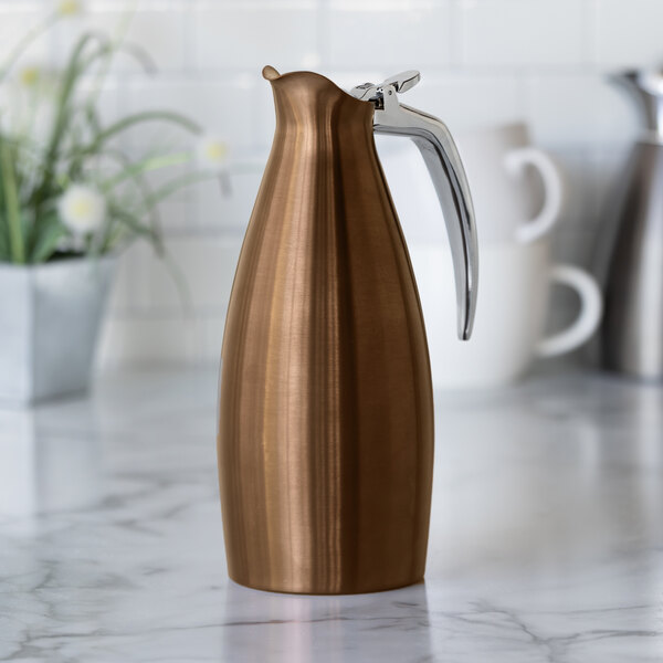 A rose gold stainless steel insulated coffee carafe server with a sleek design and a metal handle.
