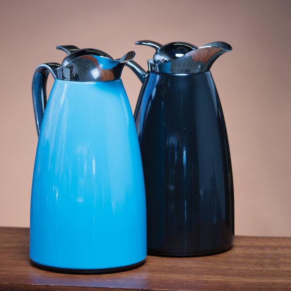 A blue powder-coated stainless steel insulated coffee carafe with a push-button lid, shown next to a black carafe.