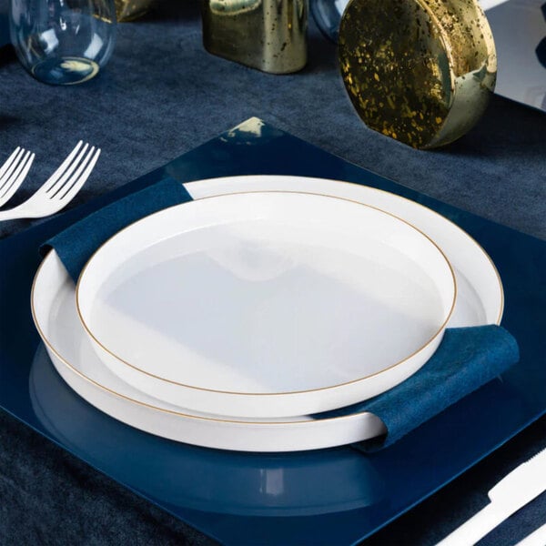 A round pearl white plastic plate with a gold band, placed on a blue square charger.