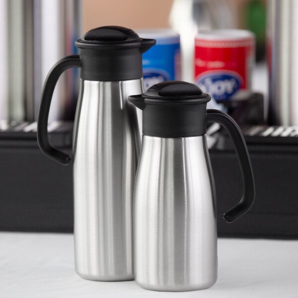 A pair of stainless steel coffee carafes with black handles and lids.