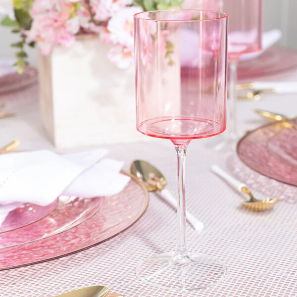 A two-toned pink and clear plastic wine goblet with a modern cylindrical shape, placed on a decorated table setting.