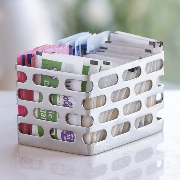 A polished stainless steel sugar packet holder containing assorted sweetener packets.