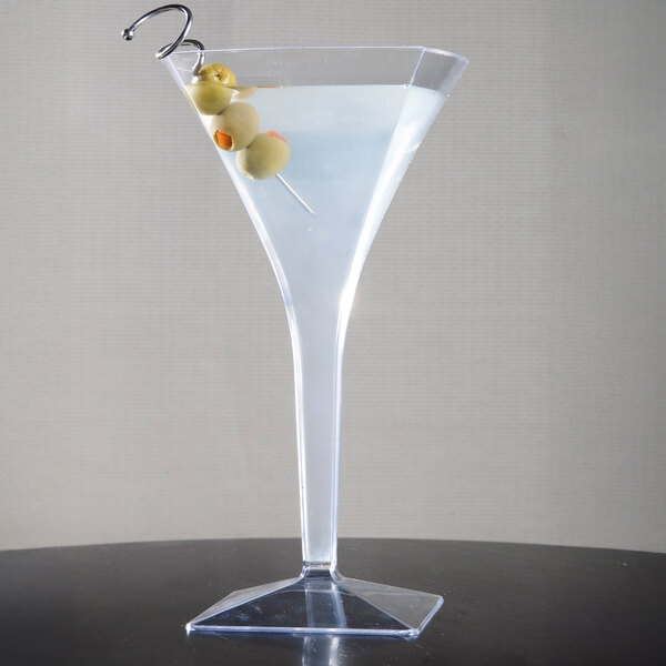 A clear disposable plastic martini glass filled with a drink and garnished with olives on a pick.