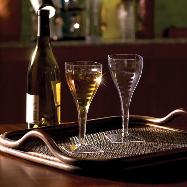 A pair of clear square plastic disposable wine glasses on a tray next to a wine bottle.