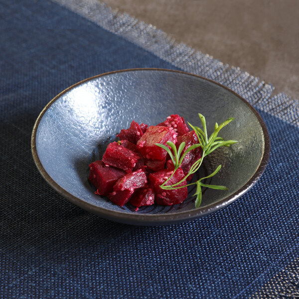 A dark blue coupe bowl containing diced red food and a sprig of green garnish.