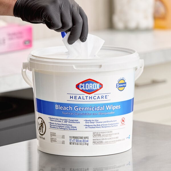 A container of Clorox Healthcare bleach germicidal wipes with a gloved hand pulling out a wipe.