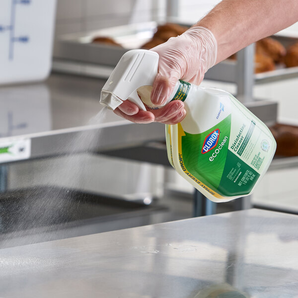 A person spraying a bottle of CloroxPro Clorox EcoClean disinfecting cleaner onto a metal surface.