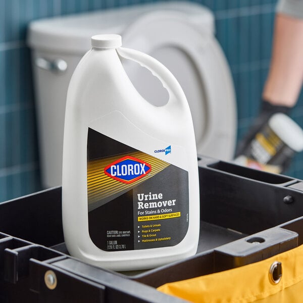 A one-gallon container of CloroxPro Clorox urine stain and odor remover placed on a cleaning cart in a restroom setting.
