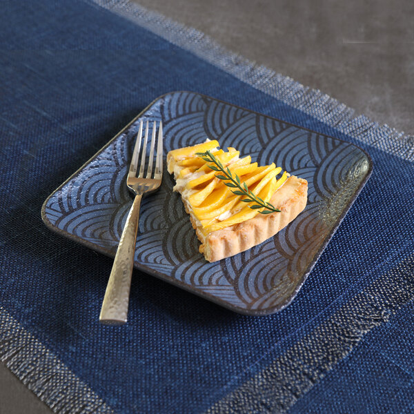 A square dark blue melamine plate with a decorative pattern, holding a slice of tart and a fork.