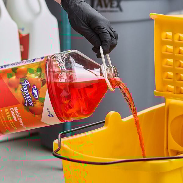 A bottle of Clorox Fraganzia citrus blossom scent multi-purpose cleaner being poured into a yellow mop bucket.