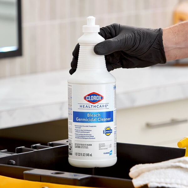 A 32 oz. bottle of Clorox Healthcare Bleach Germicidal Cleaner being held by a person wearing a black glove.