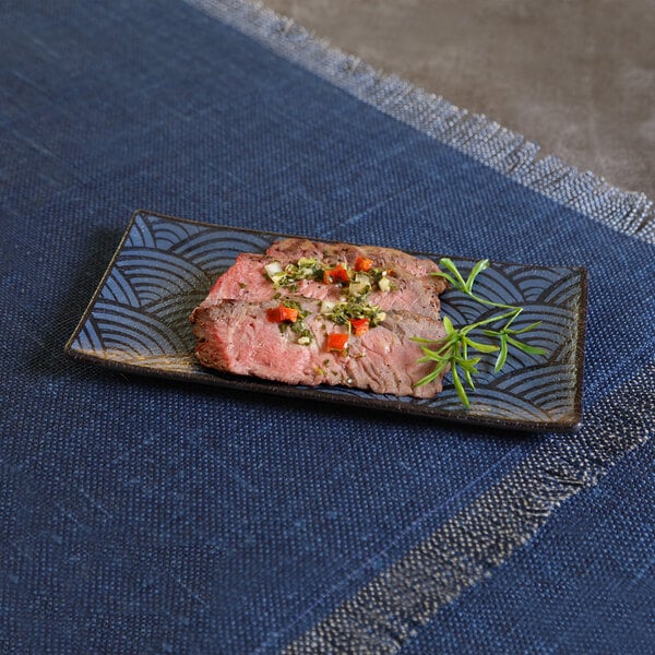 A rectangular dark blue melamine platter with a wave pattern, holding slices of garnished meat and a sprig of herbs.