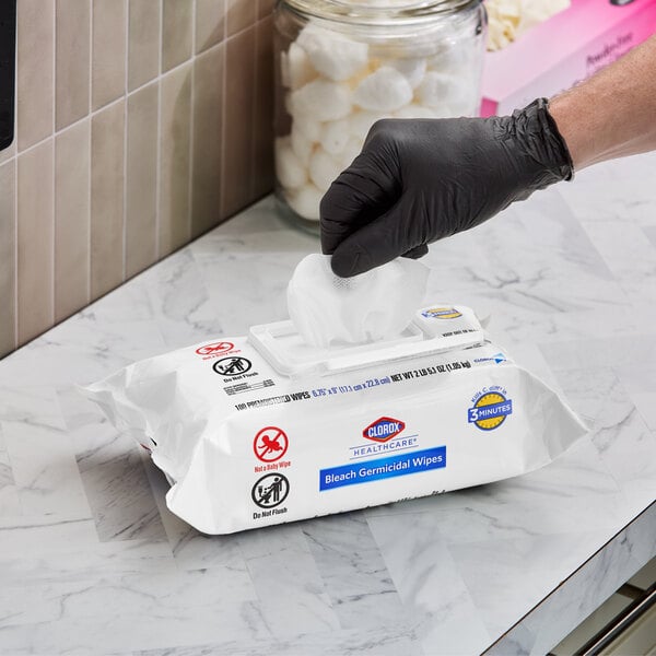 A package of Clorox Healthcare Bleach Germicidal Wipes being dispensed by a person wearing a black glove.