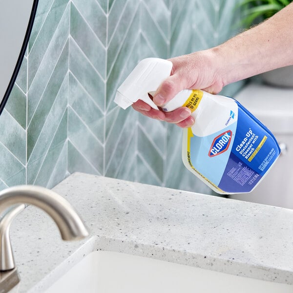 A hand holding a spray bottle of Clorox Clean-Up disinfectant cleaner with bleach near a bathroom sink.