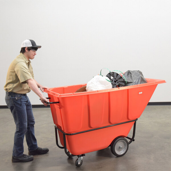 A person pushing a large red medium-duty bulk tilt truck filled with various items.