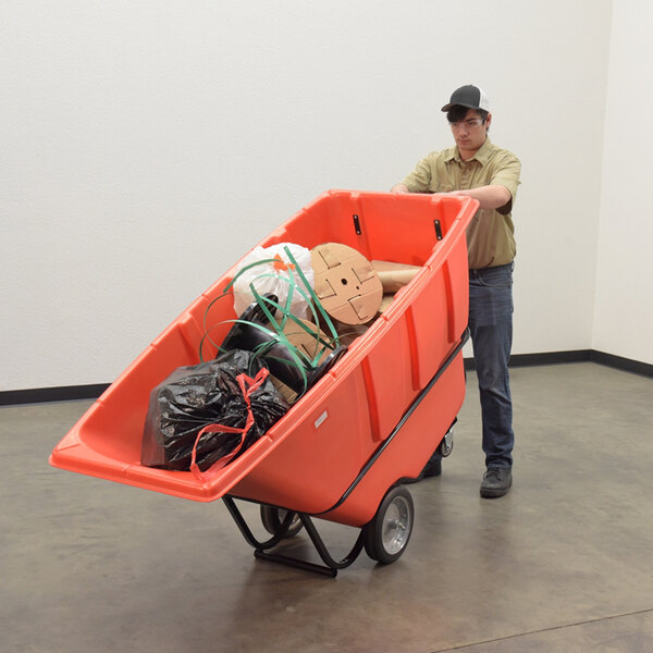 A red medium-duty bulk tilt truck filled with various items, being pushed by a person in a work uniform.