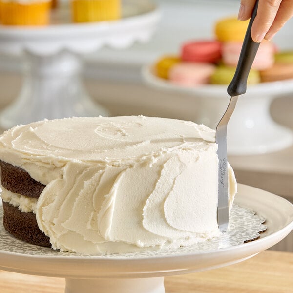 A chocolate layer cake being frosted with vanilla icing on a cake stand.