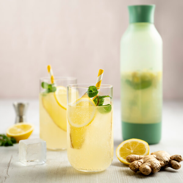 A sage green iSi Twist'N Sparkle Virtuoso 1 liter sparkling beverage system with two glasses of lemon and mint sparkling drink, fresh ginger, lemon, and ice cubes.