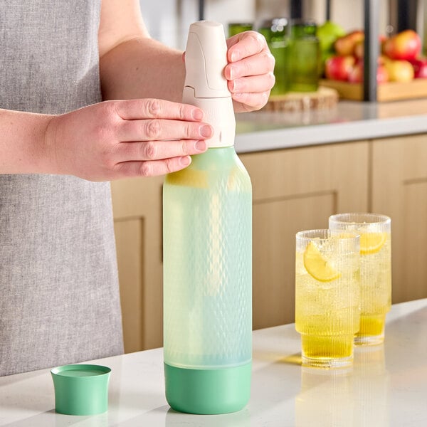 A sage-colored iSi Twist'N Sparkle Virtuoso 1 liter sparkling beverage system being used on a kitchen counter.