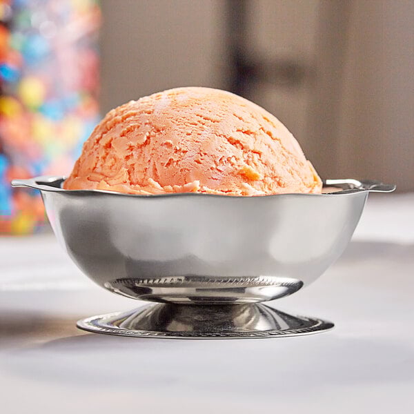 A stainless steel paneled sherbet dish holding a scoop of orange ice cream.