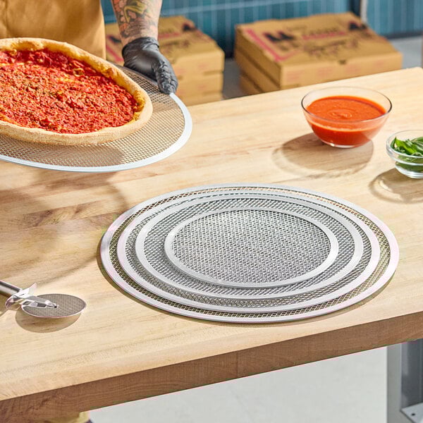 A set of round, heavy duty expanded aluminum pizza screens on a wooden countertop.