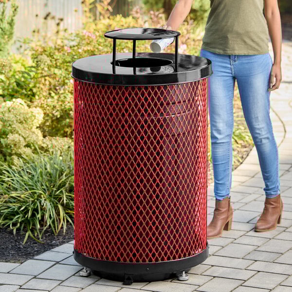 A large, round, red expanded steel outdoor trash can with a rain bonnet lid.