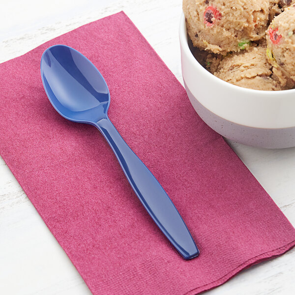 A navy blue heavy weight plastic spoon placed on a pink napkin next to a bowl of cookie dough.