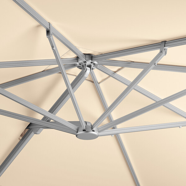 A close-up view of the frame and canopy of a square sand-colored cantilever umbrella with a silver aluminum hydraulic lift mechanism.