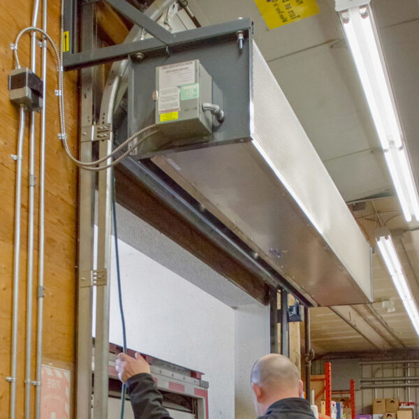 An industrial direct-drive ambient air curtain installed above a doorway in a commercial or warehouse setting.