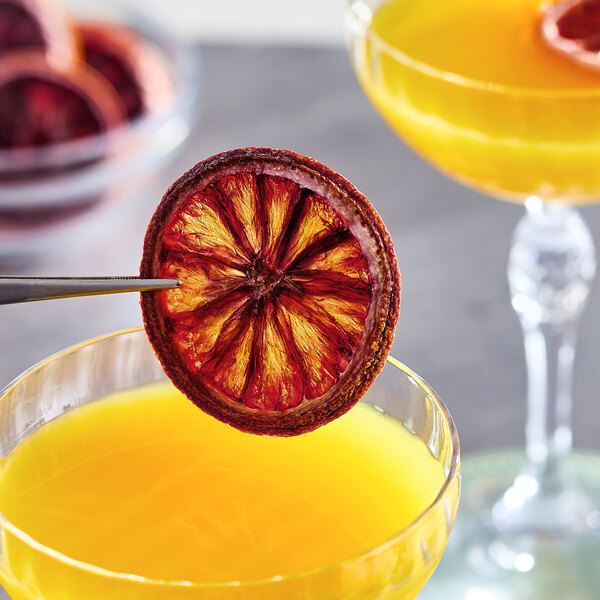 A dried blood orange slice being used as a garnish for a yellow cocktail.
