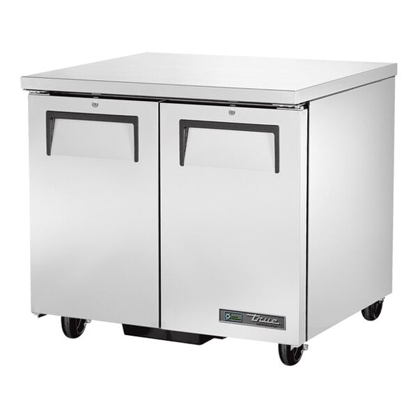 A stainless steel low-profile undercounter refrigerator with two doors and casters.