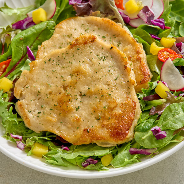 A plate of plant-based vegan chicken fillets served on a bed of mixed salad greens and vegetables.